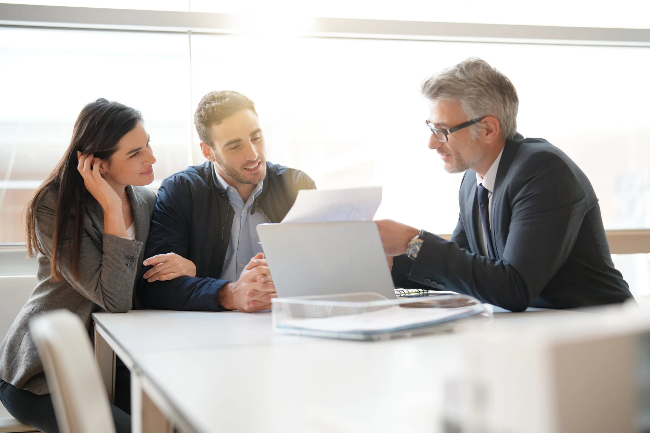 A male financial advisor speaks with a man and a woman while showing them a financial report.
