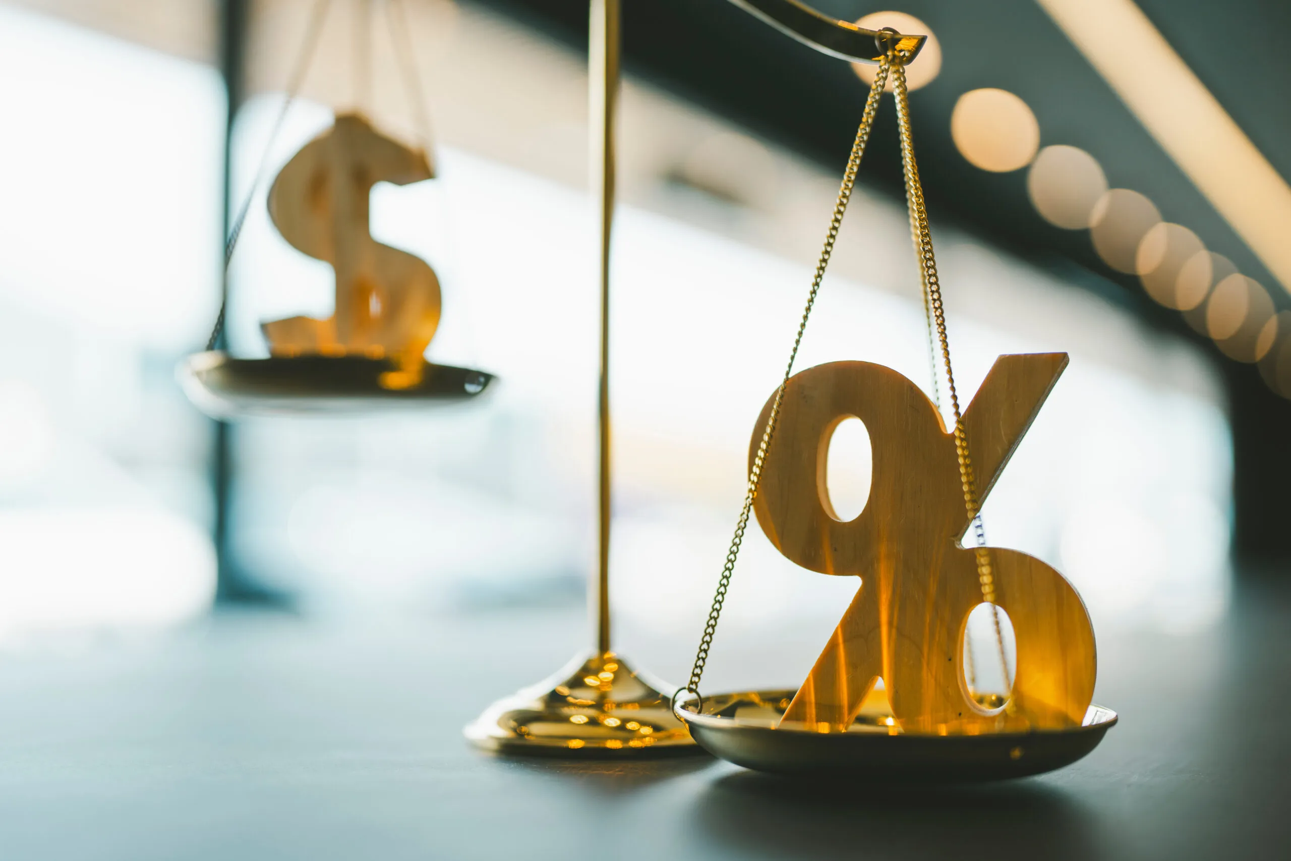 A golden percentage symbol an da golden dollar symbol sit on opposite ends of a golden scale
