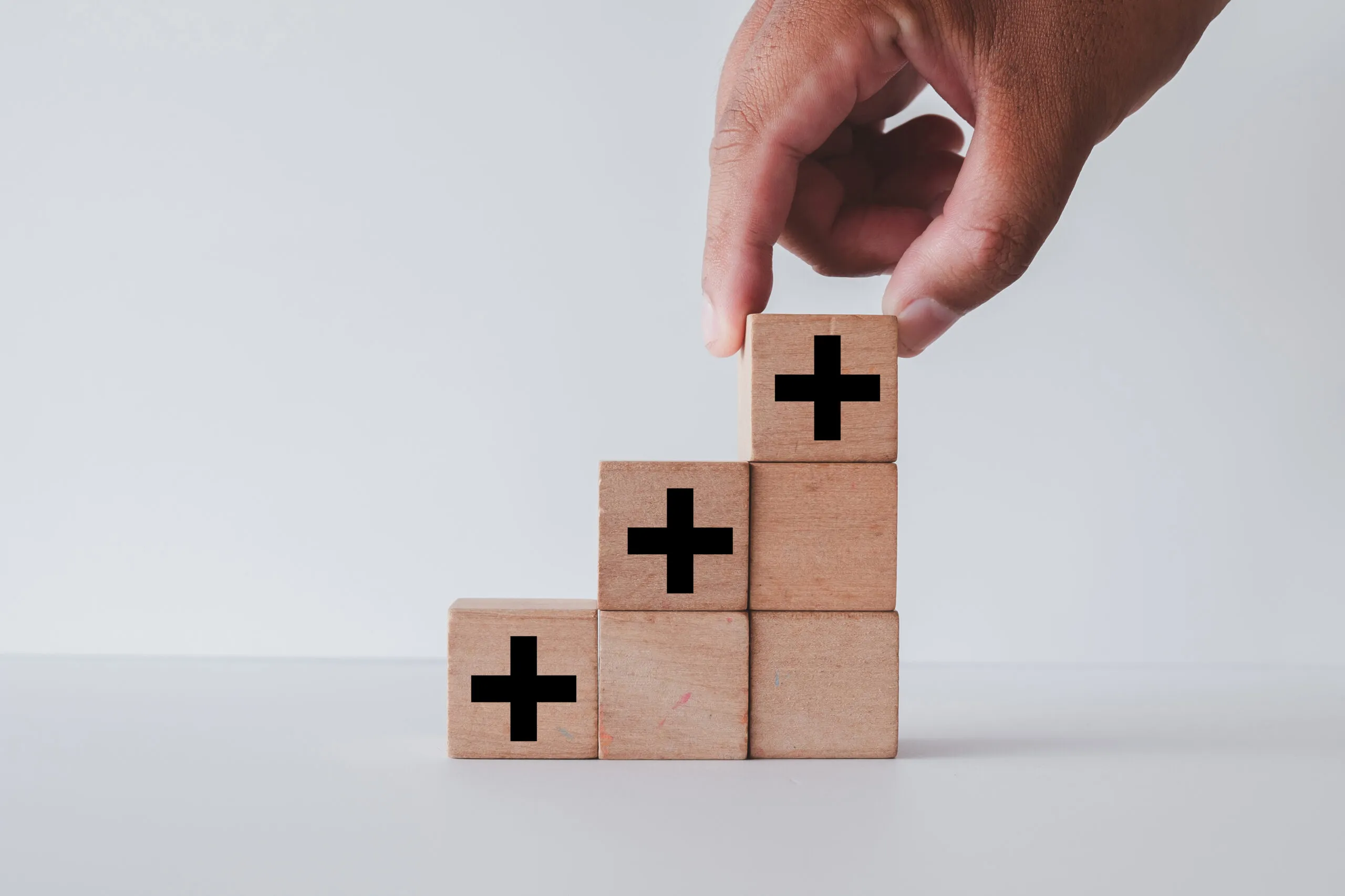 A hand grips a wooden block with a plus sign
