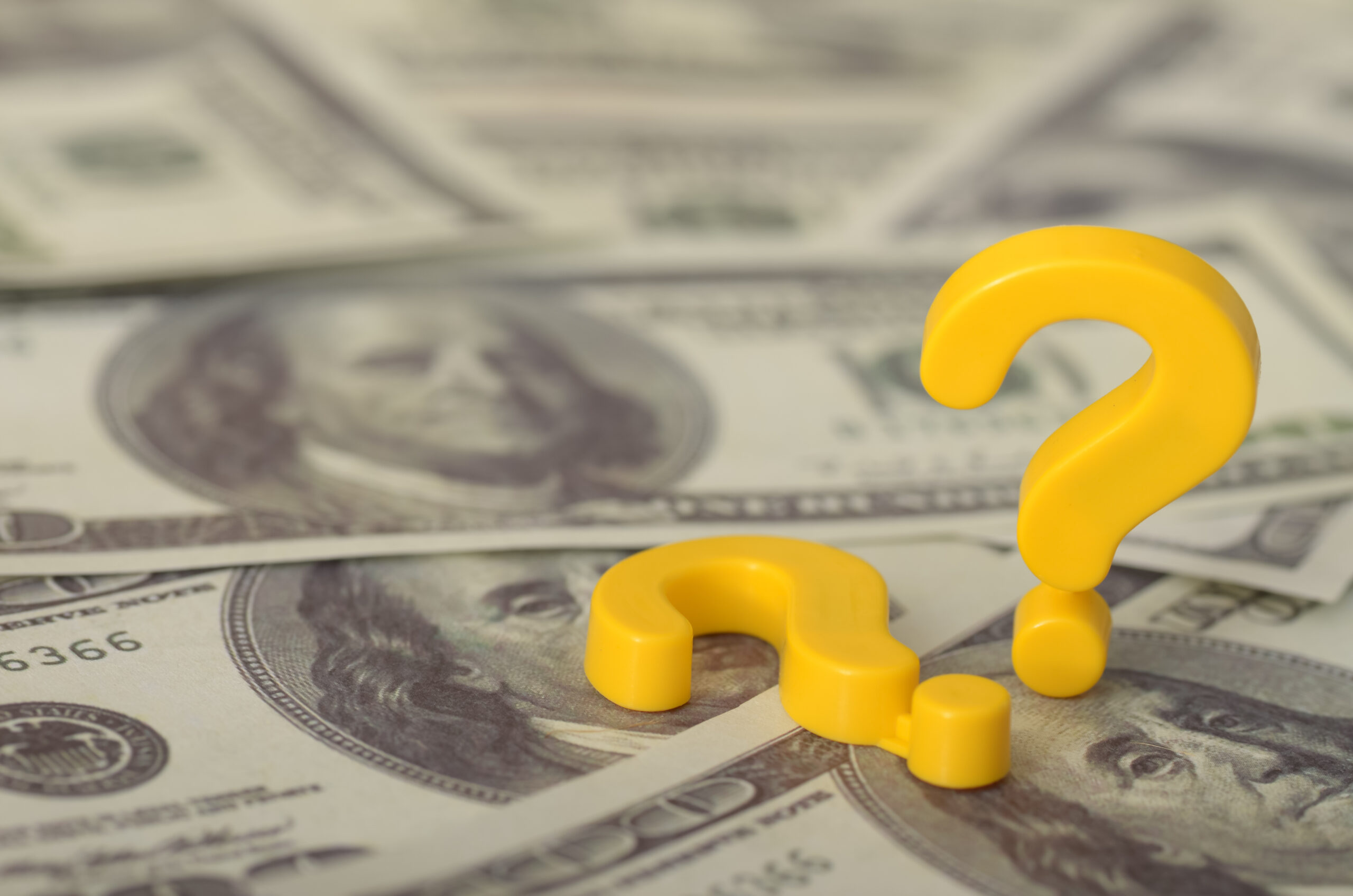 Two yellow question marks on top of hundred dollar bills