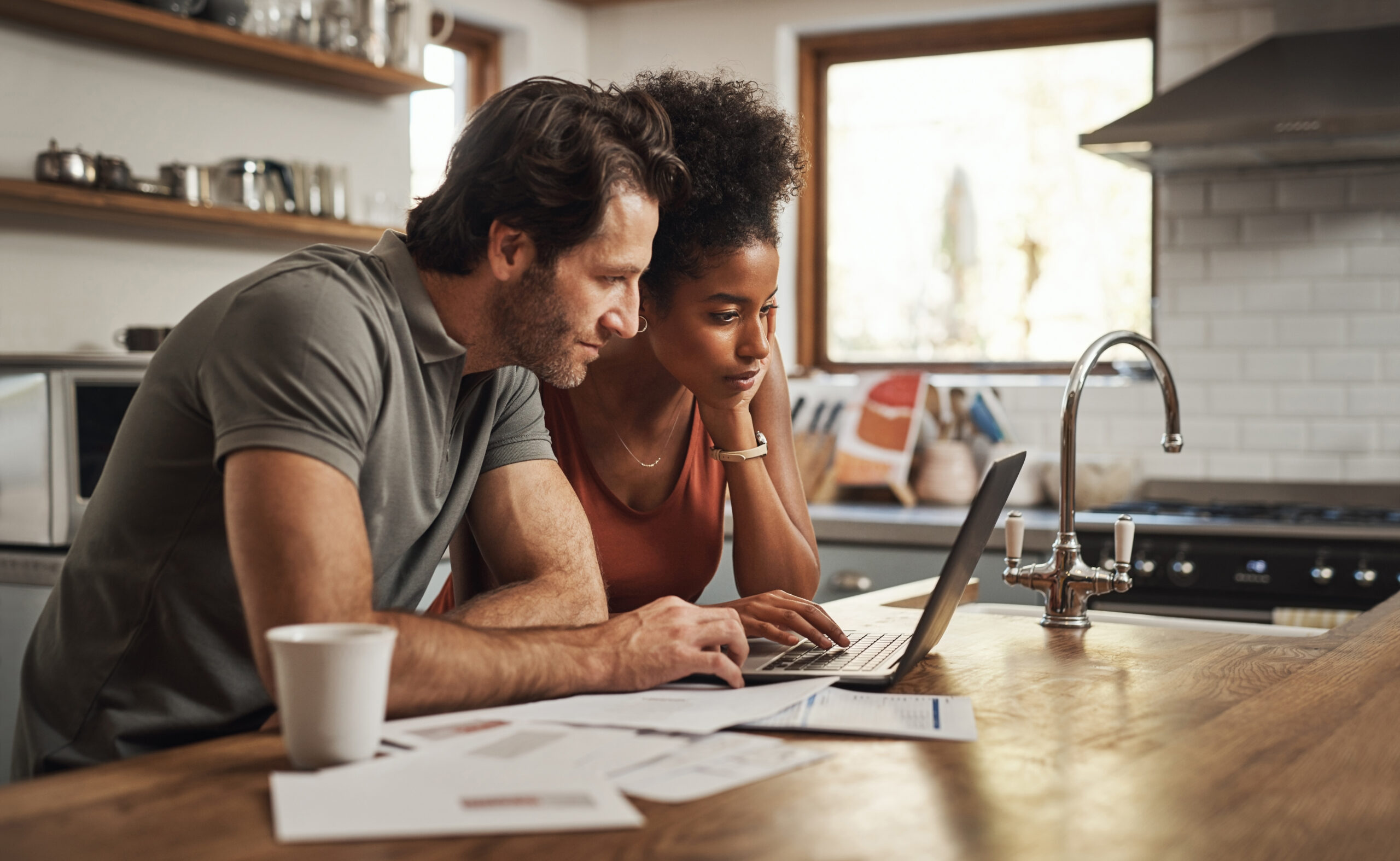 A young couple looks at a laptop together while sitting at a desk.