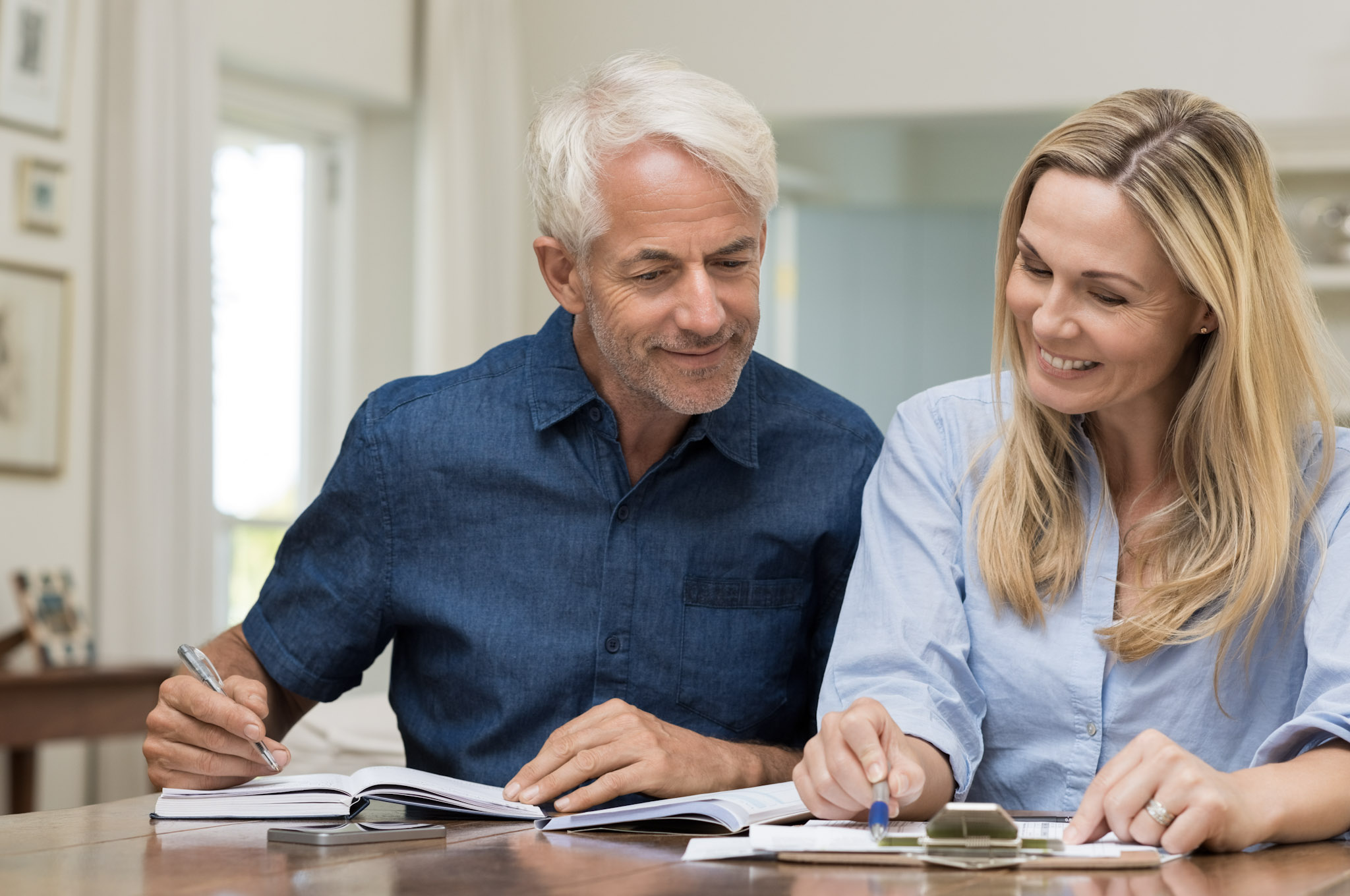 A man and woman sit at a desk, smiling while writing on a clipboard