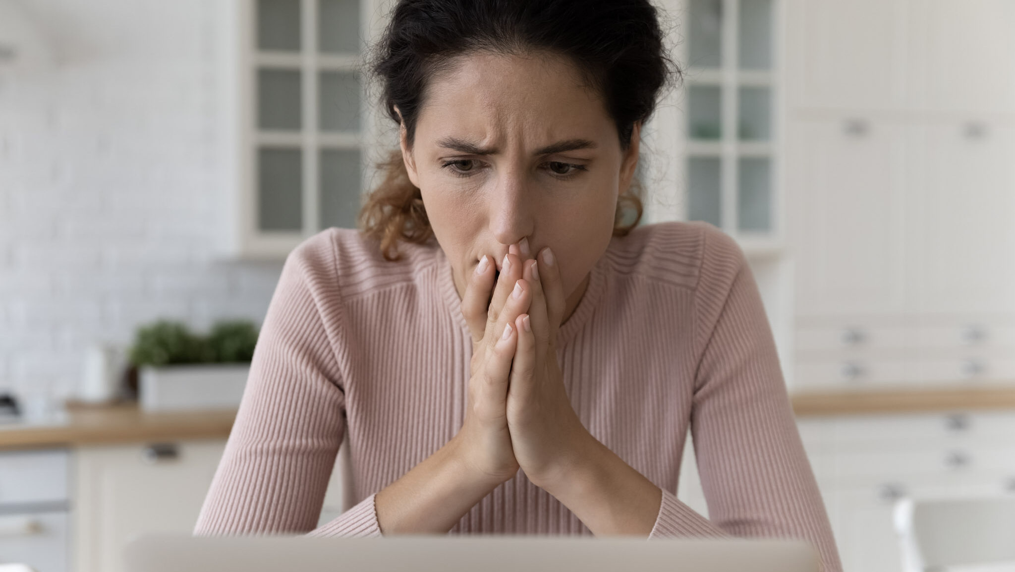 A woman in a pink sweater looks concerned while working on her computer.