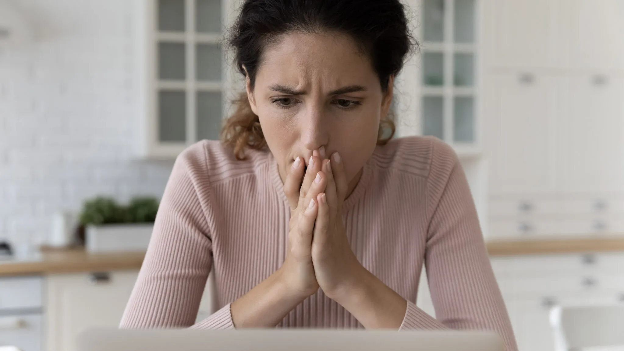 A woman in a pink sweater looks concerned while working on her computer.
