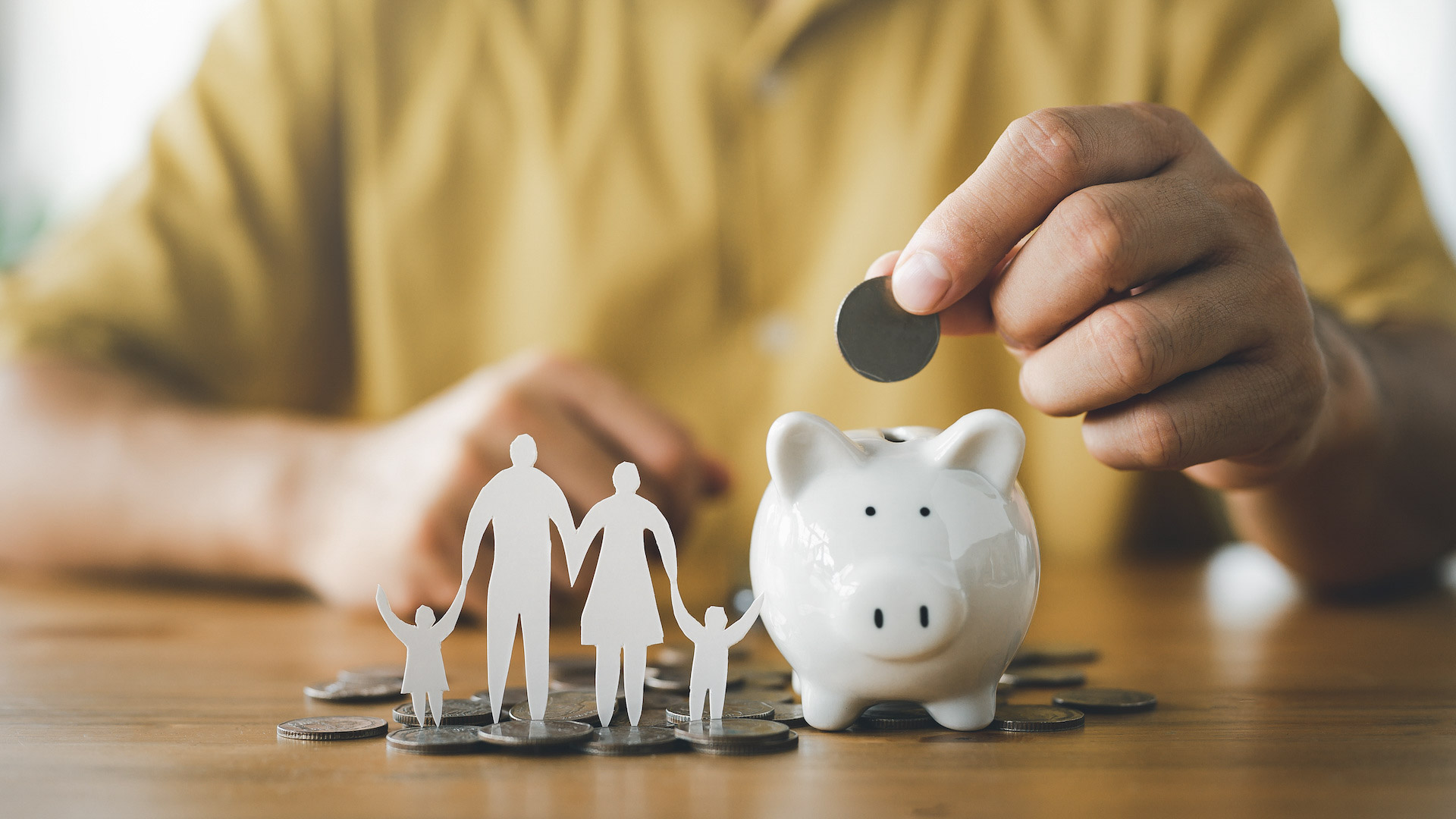 A hand places a coin inside of a small white piggy bank.