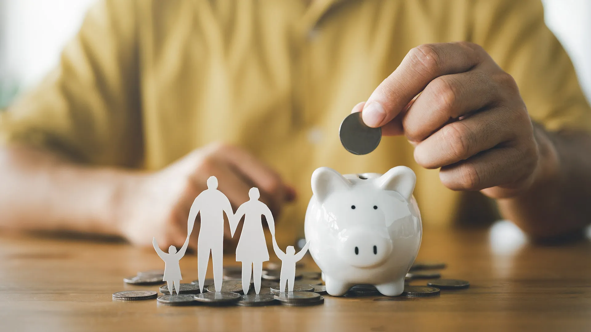 A hand places a coin inside of a small white piggy bank.