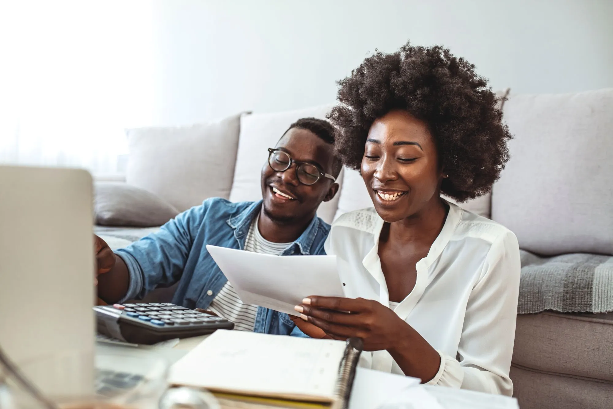 A couple sits in front of their couch while doing their finances.