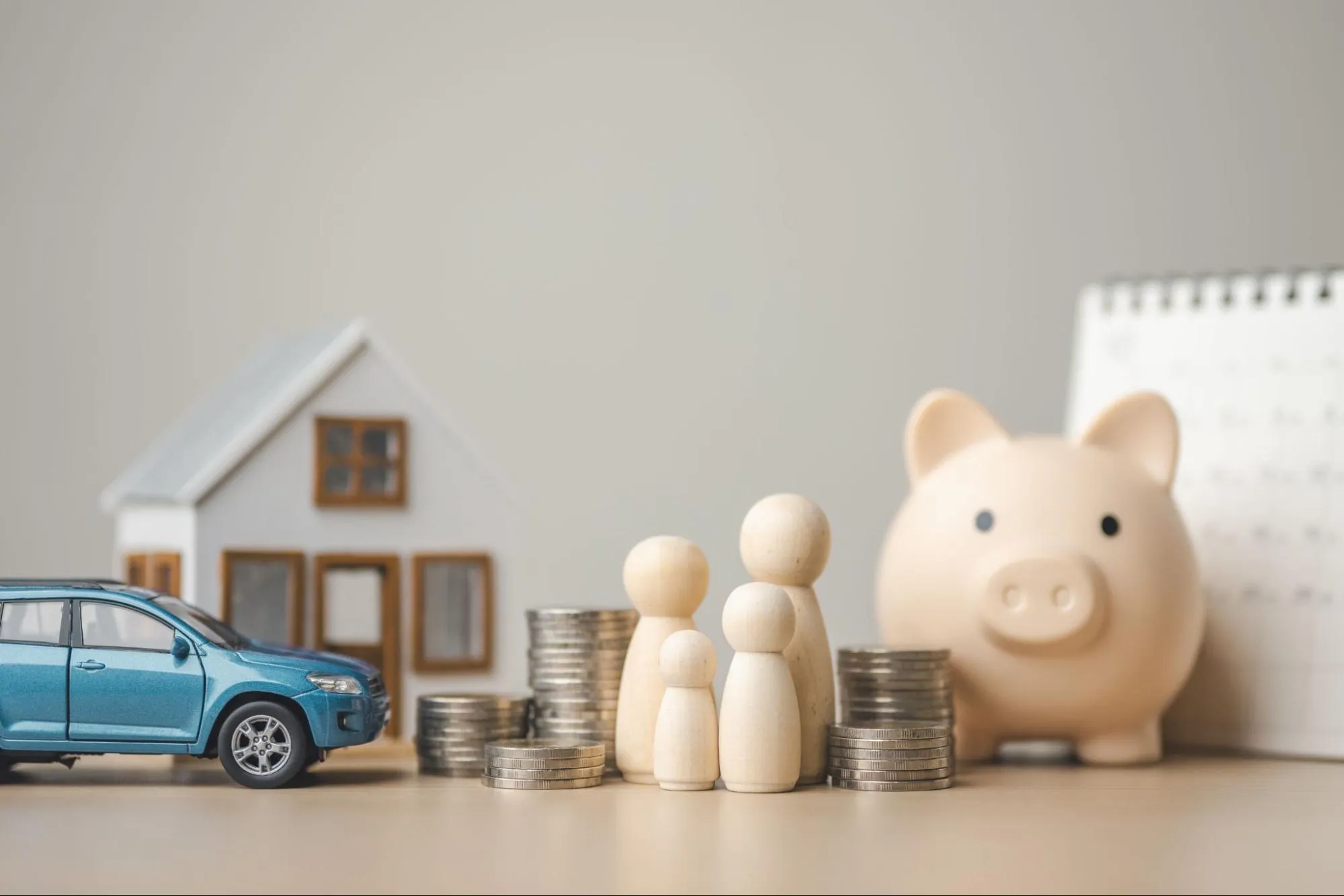 A model car, home, and family rest on a table with stacks of coins surrounding them.