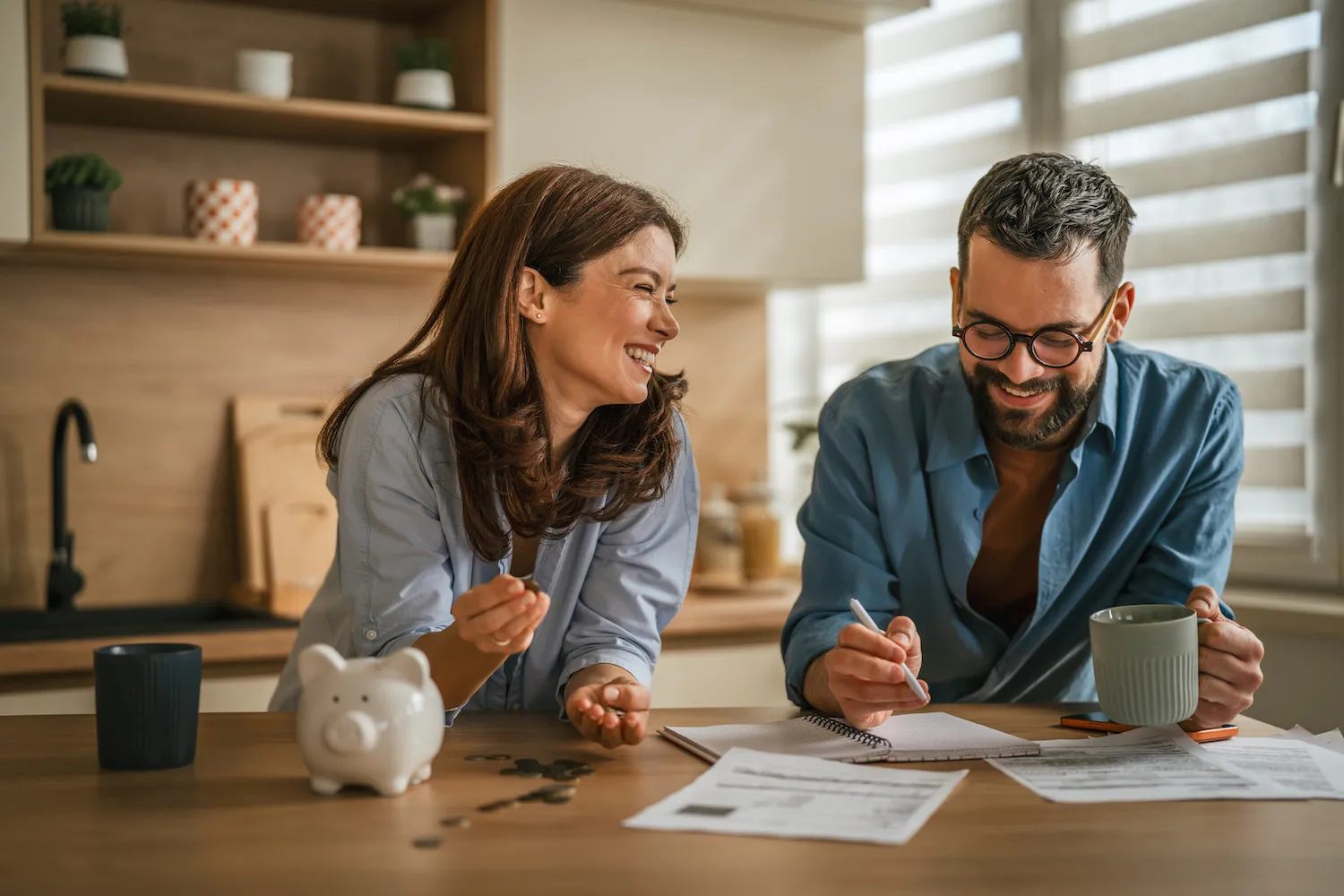 A man and woman smile while talking about finances in the kitchen