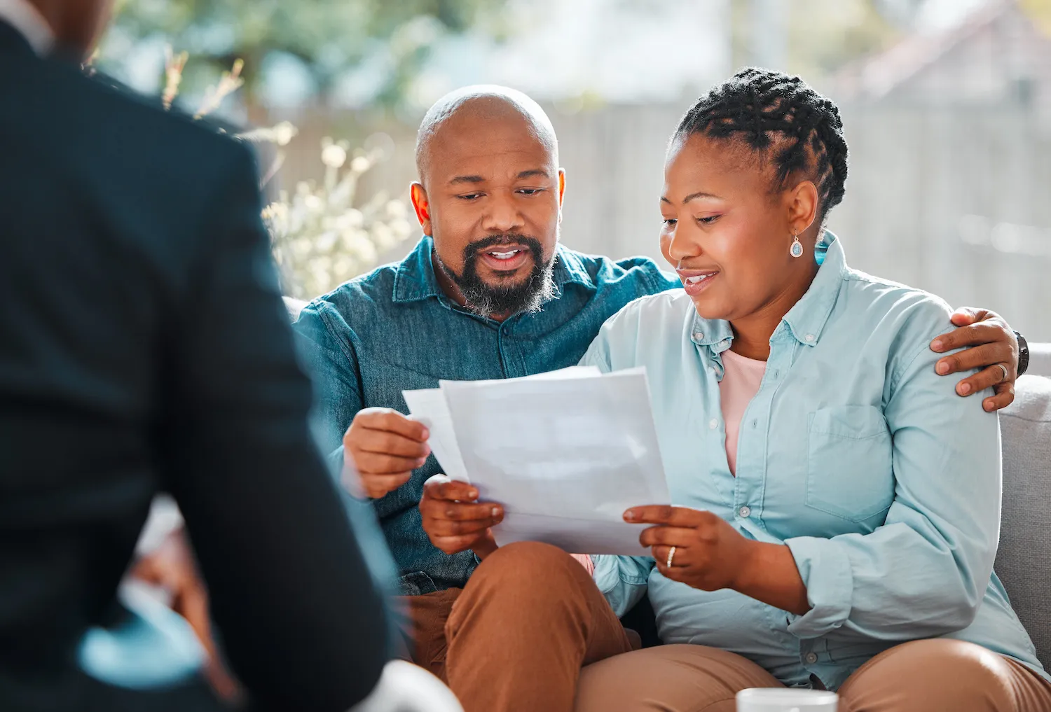 A couple sits on a couch reviewing papers while speaking with a financial advisor.